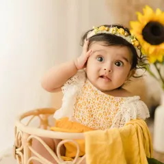A cute and funny moment from a 6-month sitter session. The baby girl makes a surprised face while sitting in a wicker basket, showing off her playful side.