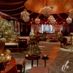 A wide view of the reception hall, blending traditional Indian opulence with modern luxury. A color palette of deep red and gold is accented with ivory florals, while dozens of chandeliers create a majestic atmosphere.