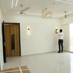 Our team member is installing modern wall lights in a spacious, empty living room. This image shows the blank canvas before furniture, highlighting the importance of getting the lighting and electricals right from the start.