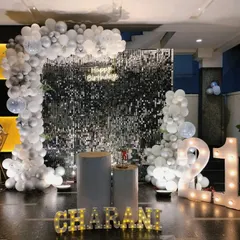 A stylish 21st birthday setup with a black shimmer wall, an all-white balloon arch, and illuminated marquee numbers and letters spelling out a name.