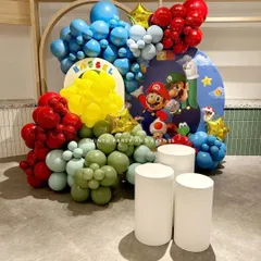 A colorful Super Mario themed birthday setup with balloon clusters representing the game's iconic colors and characters like Mario and Luigi on the backdrop.