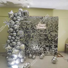 Make your birthday unforgettable with a glamorous silver sequin wall backdrop. This party setup creates a perfect photo booth, featuring a cascade of chrome silver balloons, disco balls, star-shaped foil balloons, and a bright "Happy Birthday" neon sign.