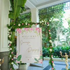 A beautiful welcome sign for Saumya and Digvijay's wedding. The sign is framed with a delicate arch of fresh greenery and pink and white roses, perfectly matching the event's floral theme.