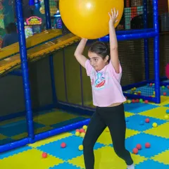 A girl showing her strength while playing with a large yoga ball in the play area.