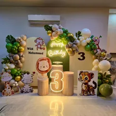 This 'Wild Mohammed' jungle theme setup is perfect for a third birthday. It features cute animal cutouts, a 'Happy Birthday' neon sign, a light-up marquee number '3', and a sophisticated balloon arrangement in earthy tones.