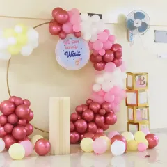 A beautiful baby shower decoration in a Sarjapur Road apartment. This ring balloon decor with pastel pink, chrome, and yellow balloons and a "We Can Barely Wait" sign creates the perfect photo spot for the parents-to-be.