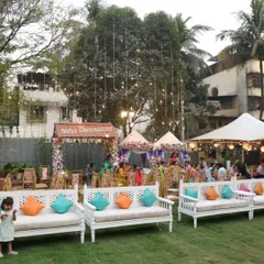 This outdoor Mehendi setup was designed for a relaxed and festive daytime celebration. We arranged comfortable seating with colorful cushions, tents for shade, and decorative stalls under beautiful string lights hanging from the trees.
