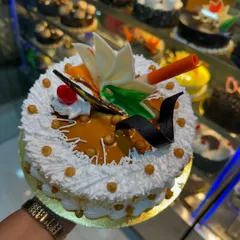 A classic Butterscotch cake, held up to show its beautiful decoration. It's topped with caramel glaze, butterscotch crunchies, and delicate white and dark chocolate garnishes.