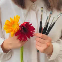 A close-up on the hands of the artist, holding flowers and brushes.