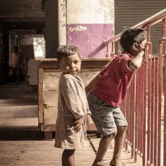A candid street photograph of two young children looking out from a balcony, capturing a moment of childhood innocence and curiosity.
