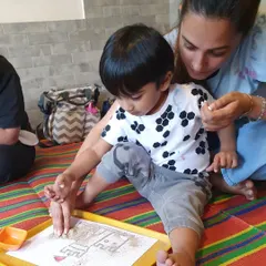 A parent helping her child with a sand art project. These activities are great for developing fine motor skills as they carefully pour sand onto their designs.