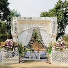 Sun-kissed simplicity meets royal elegance. This Haldi setup features an intricate ivory jaali backdrop, soft drapes, and bursts of pastel florals, creating a look of understated grace and cultural charm.