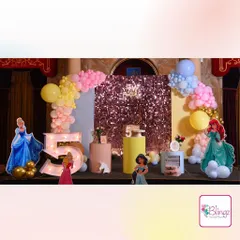 A grand Disney Princess stage for a 5th birthday celebration. The setup includes a sparkling rose gold sequin backdrop, life-sized cutouts of Cinderella and Ariel, and a light-up marquee number '5'.