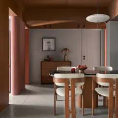 A focused view of the dining set, highlighting the clean lines of the wooden chairs and the smooth, dark tabletop. The terracotta curved wall in the background adds a touch of earthy color.