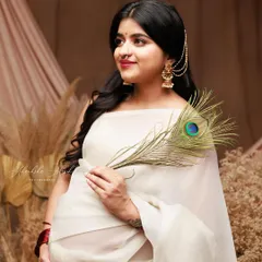 An ethereal portrait in a simple white saree, accented with traditional gold jewelry and a peacock feather. This look is a beautiful blend of modern minimalism and cultural elegance.