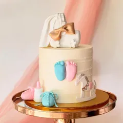 This gender reveal cake features pink and blue baby feet, a rocking horse, and a bassinet topper. The details are handcrafted from fondant.