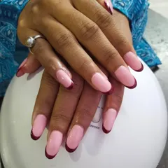 A modern take on the French manicure with bold, deep red tips on rounded gel extensions. The contrast between the pink base and the dark tips creates a very chic and sophisticated look.