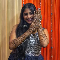 A happy client showing off her stunning bridal mehndi. The design features dense patterns, including geometric checks and floral bands, creating a rich and textured look perfect for a bride.
