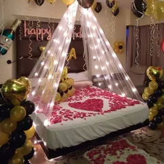 Another view of the black and gold romantic room decoration. You can see the 'Happy Birthday' foil letters, a champagne bottle balloon, and rose petals on the floor, adding to the celebratory feel.