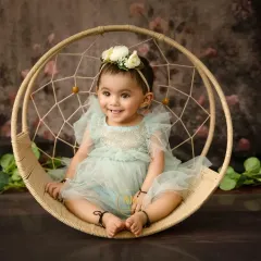 A smiling baby girl sits in a dreamcatcher-style swing, a popular prop for sitter sessions.