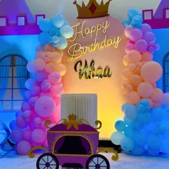 A charming princess carriage theme for Vihaa's 5th birthday. The backdrop includes a neon "Happy Birthday" sign, a crown, and a cute carriage prop, all surrounded by pastel pink, orange, and blue balloons.