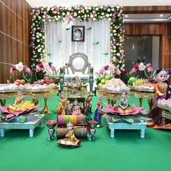 A classic South Indian Seemantham setup. The decor features an elegant floral arch, a traditional silver chair for the mother-to-be, and an elaborate display of fruits and sweets on decorated plates.