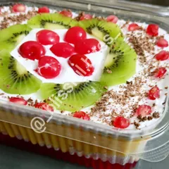 A close-up of my classic Mixed Fruit Trifle, beautifully decorated with fresh kiwi, cherries, and pomegranate seeds. This dessert features layers of jelly, custard, cake, and cream for a delightful finish to any meal.