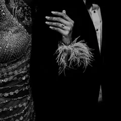 A detailed black and white shot of the couple's hands and attire, focusing on the textures of the bride's sequined dress and feathered sleeves.