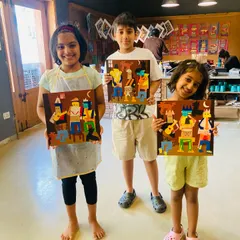 Three young artists proudly present their finished Picasso-inspired collage artworks. They learned how to deconstruct and reassemble shapes to create these cubist-style scenes.