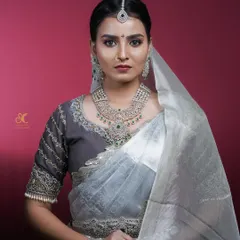 A stunning studio portrait for a makeup artist's portfolio, showcasing a 'Muhurtham' bridal look. The clean background and professional lighting emphasize the intricate details of the makeup and jewelry.