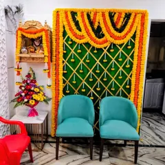 A vibrant setup for a house pooja in Vile Parle. We created a backdrop with orange and yellow marigold garlands against a green panel, perfectly complementing the small wooden home mandir.