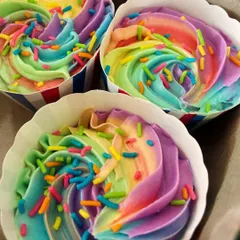 A close-up of three rainbow cupcakes in a box. The vibrant swirls of frosting are perfect for celebrating Pride Month or any happy occasion.