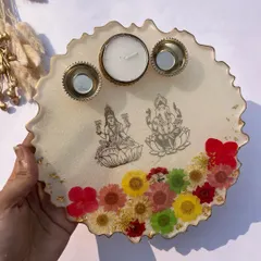 A beautiful Diwali gift idea. This is a resin platter with images of Lakshmi and Ganesha, decorated with real dried flowers and featuring candle holders.