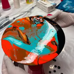 A participant holding up their freshly poured fluid art creation. The combination of orange, turquoise, and black came out so beautifully in this piece.