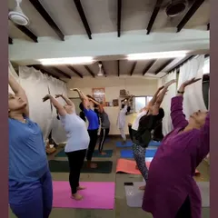 Students in a group class moving through a gentle backbend, raising their arms to open the chest and shoulders. Each person is encouraged to move within their own range of motion.