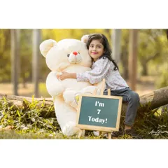 A sweet smile for her seventh birthday. Brishka hugs her giant teddy bear next to a sign announcing her big day. This portrait combines a classic prop with a genuine, happy expression.
