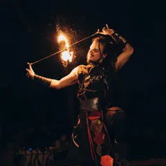 A male fire performer kneels while spinning a fire poi, creating a shower of sparks. This shot highlights the spiritual and focused nature of our fire art.