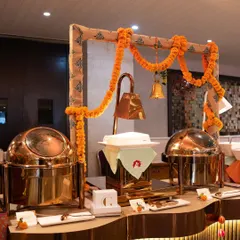 A traditional buffet setup featuring gleaming copper chafing dishes under a frame decorated with marigold garlands and temple bells. This design evokes a sense of heritage and festive celebration.
