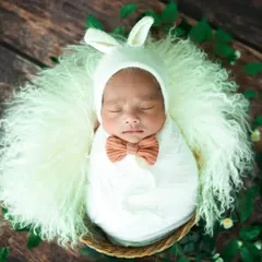 Dressed up and ready for a nap. This baby looks adorable in a white bunny-ear bonnet and a little bow tie, nestled in a fluffy basket.