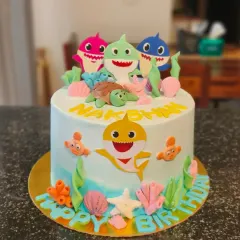 An adorable Baby Shark cake featuring fondant sea creatures and the whole shark family. The light blue ombre effect mimics the ocean.