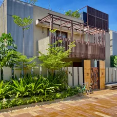 The street-facing facade of a home at Udyāna. The interplay of corrugated surfaces, wooden screens, and dense foliage creates a rich textural experience and a sense of privacy.