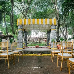 A wider view of the temple-inspired mandap at Angana the Courtyard. The symmetrical arrangement of the golden Tiffany chairs and the floral canopy creates a grand and inviting aisle for the wedding procession.