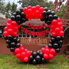 A full-circle balloon ring in bold red and black, set up in a garden. This makes a striking photo backdrop against the natural greenery.