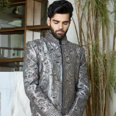 A masterpiece in gunmetal silk, this sherwani is elevated with intricate all-over threadwork. The sculpted shoulders and textural cuffs create a powerful blend of regality and modern edge, perfect for a groom or for making a statement at a grand event.