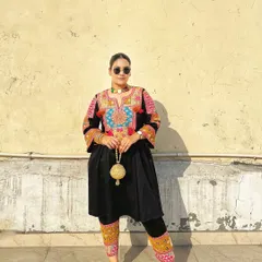 I love how the sunlight catches the texture of this handcrafted golden potli, highlighting its spherical shape and delicate details against the dark, embroidered outfit.