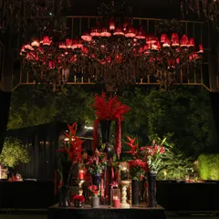 A stunning red-shaded chandelier hangs over a lavish floral arrangement. This image showcases our use of bold color and statement lighting to create a powerful and cohesive theme.