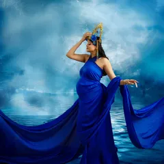 Standing like a sea goddess, this mother-to-be exudes strength and serenity. The flowing blue fabric and stormy backdrop create a dramatic and powerful contemporary portrait.
