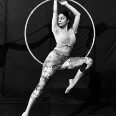A student strikes a dynamic, poised pose on the aerial hoop. This black and white shot highlights the elegant lines and muscular engagement required.