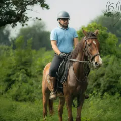Fully equipped for a safe and enjoyable ride. This rider, wearing a helmet and gloves, is ready to explore the green trails on one of our well-trained brown horses.