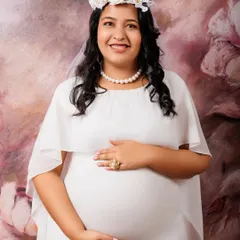 Sometimes, simplicity is the most elegant statement. This classic maternity portrait features a beautiful mother-to-be in a simple white gown and a delicate floral headpiece. The focus is entirely on her serene expression and the miracle she is creating.